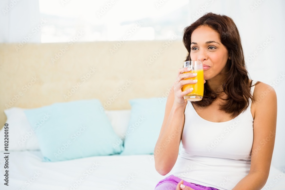 Happy woman holding glass of orange juice while sitting on bed Happy woman holding glass of orange juice while sitting on bed
