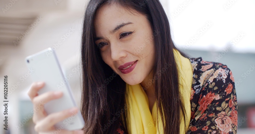 Attractive stylish young woman reading a message on a mobile with a quiet smile and look of concentration close up head shot Attractive stylish young woman reading a message on a mobile with a quiet smile and look of concentration close up head shot