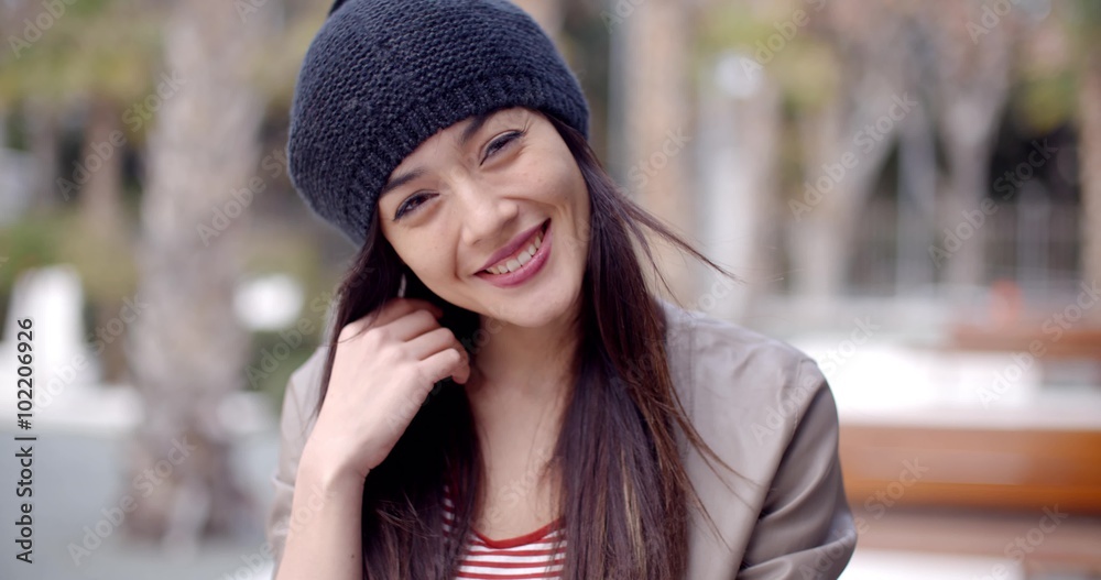 Pretty thoughtful young woman with long brown hair in a woolly cap looking at the camera with a gentle smile head and shoulders portrait Pretty thoughtful young woman with long brown hair in a woolly cap looking at the camera with a gentle smile head and shoulders portrait