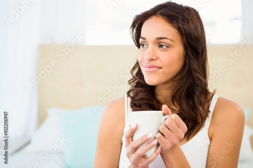 Happy woman holding cup of coffee while sitting on bed