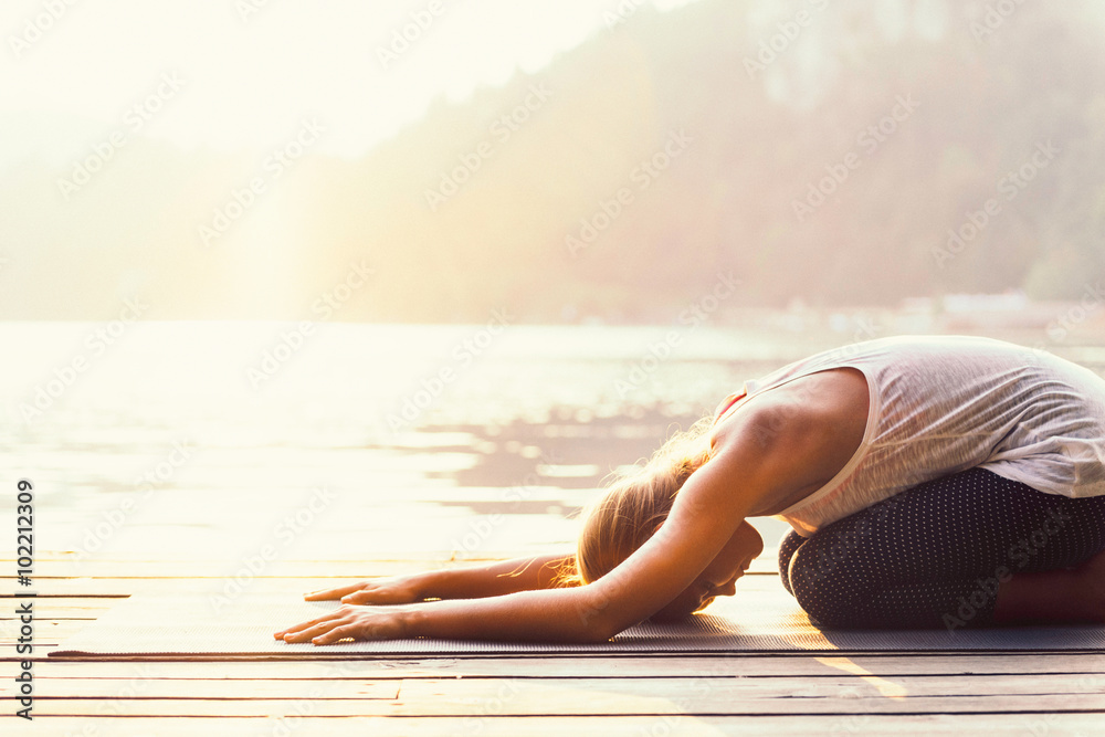 Sun salutation yoga. Young woman doing yoga by the lake, bathing in sunlight. - obrazy, fototapety, plakaty 