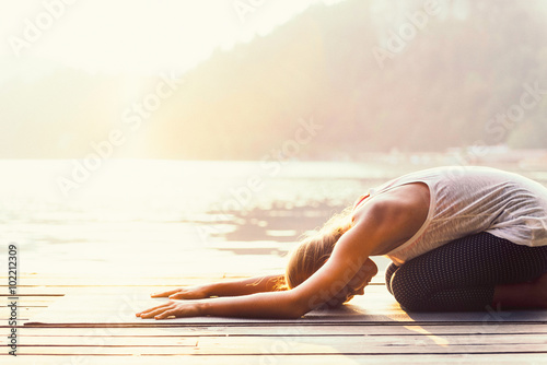 Fototapeta Naklejka Na Ścianę i Meble -  Sun salutation yoga. Young woman doing yoga by the lake, bathing in sunlight.