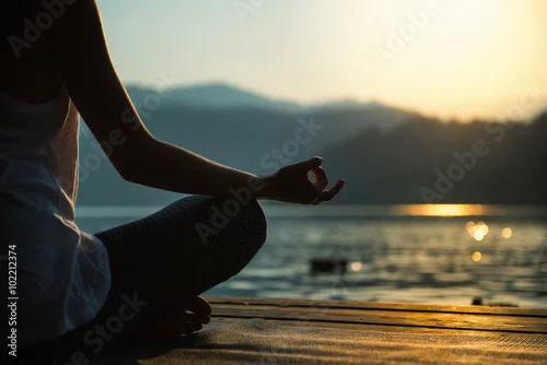Fototapeta na wymiar Meditation by the lake. Silhouette of a young woman meditating by the lake at sunset