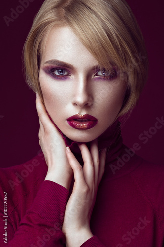 Beautiful blonde woman in a red sweater with bright makeup and dark lips. Beauty face. 