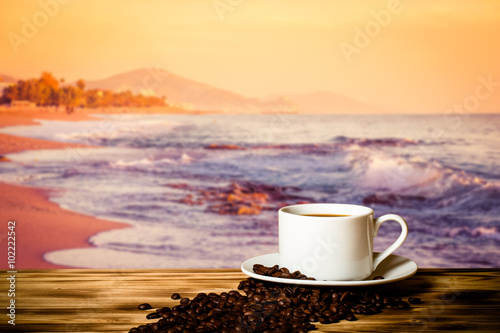 Coffee beans and coffee in cup on wooden table opposite a blurre photo