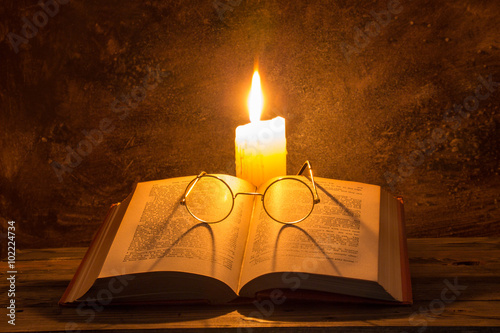 Open old book with reading glasses and candle