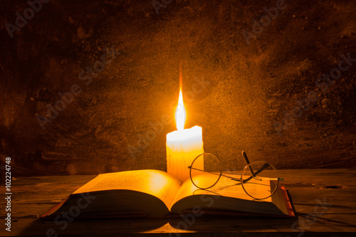 open old book with reading glasses and candle