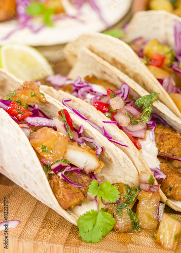 Baja Fish Tacos - Soft shell tacos filled with seasoned fried white fish served with red cabbage, pineapple salsa, chunky guacamole and creamy Baja style sauce.
