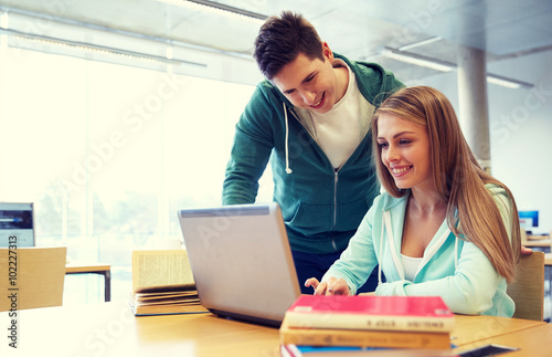 happy students with laptop in library © Syda Productions