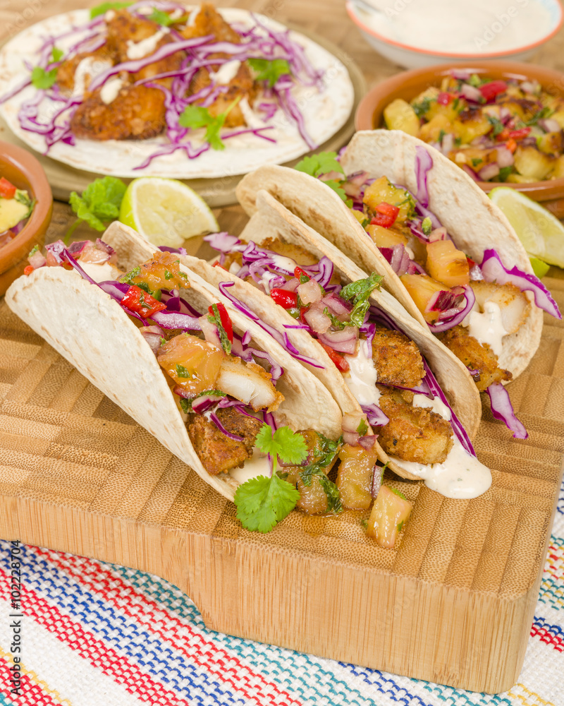 Fototapeta premium Baja Fish Tacos - Soft shell tacos filled with seasoned fried white fish served with red cabbage, pineapple salsa, chunky guacamole and creamy Baja style sauce. 
