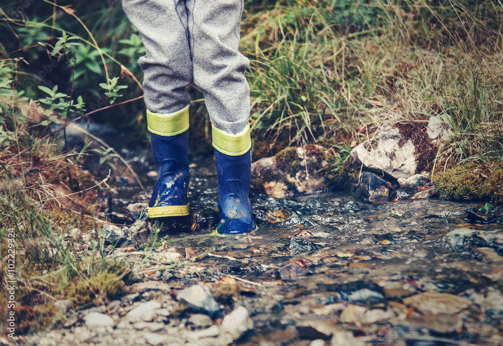 Child legs in gum boots into the forest creek Child legs in gum boots into the forest creek