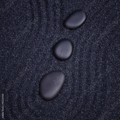 3 black stones aligned in a straight line with waves in a the ze