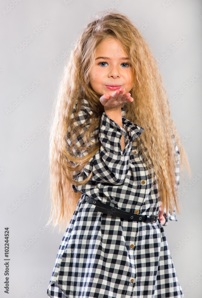 Smiling little girl standing on the gray background. Positive emotional little girl with long healthy hair and a sweet smile posing at the camera on a gray background Smiling little girl standing on the gray background. Positive emotional little girl with long healthy hair and a sweet smile posing at the camera on a gray background