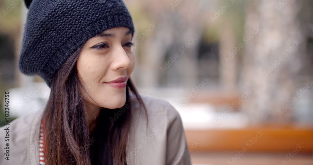 Cute single adult Asian woman in long hair and knitted hat smiling as she looks to the side Cute single adult Asian woman in long hair and knitted hat smiling as she looks to the side