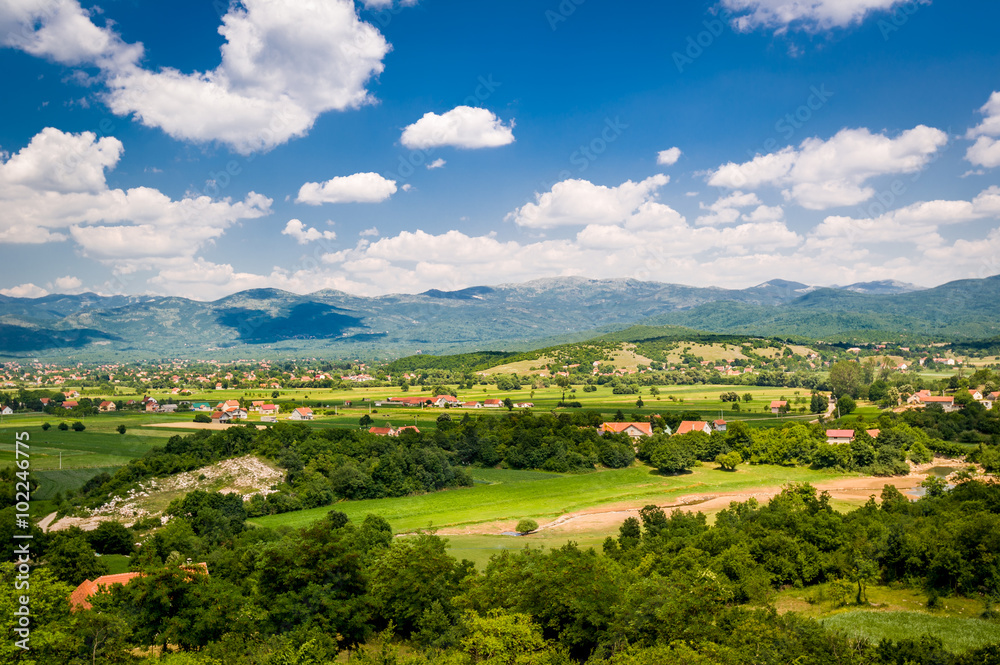 Typical Montenegrin rural landscape. Village houses in the fields, small river and mountain range on a background. Niksic, Montenegro.