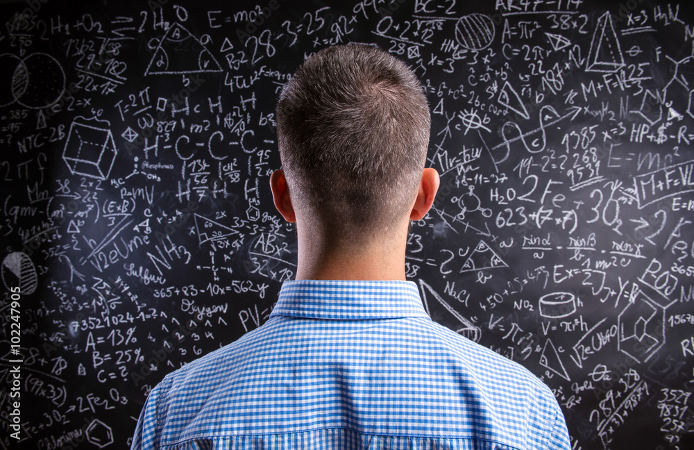 Back view of teacher against big blackboard with mathematical sy Back view of teacher against big blackboard with mathematical sy