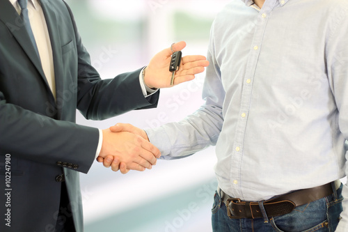 Car salesman handing over the keys for a new car to a young busi