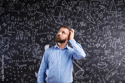 Billede på lærred Teacher scratching his head against big blackboard with mathemat