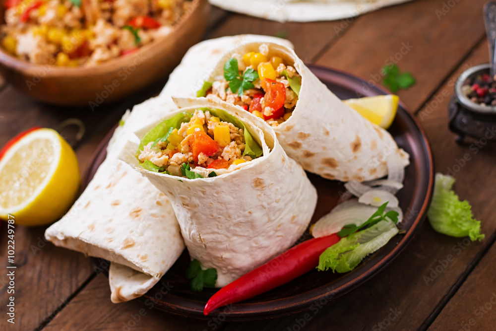 Burritos wraps with chicken meat, corn, tomatoes and peppers on wooden background Burritos wraps with chicken meat, corn, tomatoes and peppers on wooden background