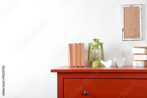 Room interior with red wooden commode  lantern and books on light wall background