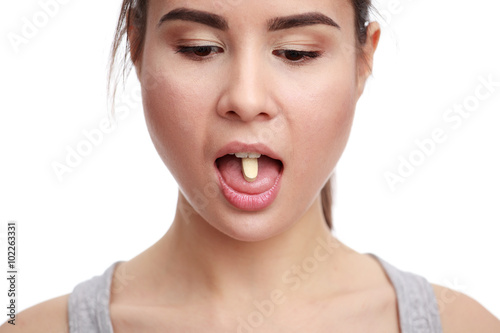 Young woman taking a tablet. The girl's face close up with a pill on the tongue.