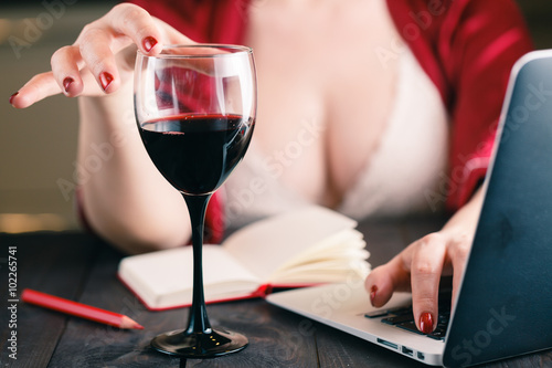 Woman touching glass of red wine and using his laptop