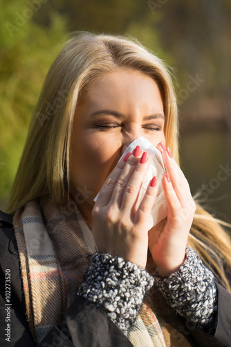 junge blonde Frau niest ins Taschentuch 