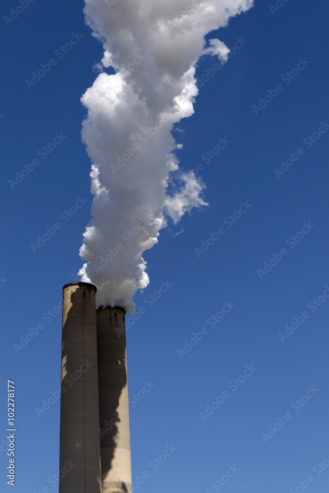 White smoke coming out of power plant chimneys on blue sky background White smoke coming out of power plant chimneys on blue sky background