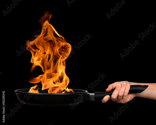 Photography Woman's hand holding a frying pan with flames on black background
