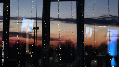 Blue tv screens reflected on big decorated windows. Picture of beautiful red sunset is behind the glass.  photo