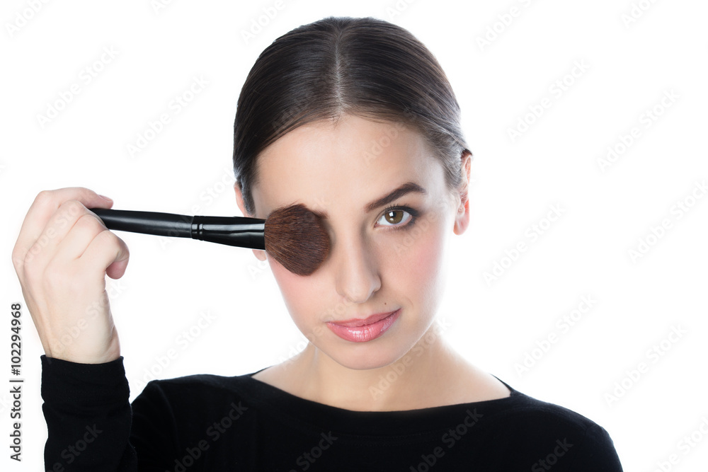 Beautiful woman holding a powder brush near her face, studio white Beautiful woman holding a powder brush near her face, studio white