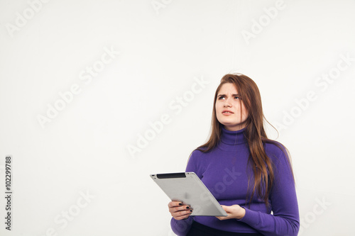 Young and beautiful teenager girl holding an ipad tablet pc in her arms over grey background