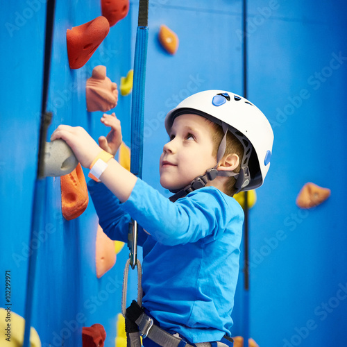 Little boy is climbing in sport park on blue wall