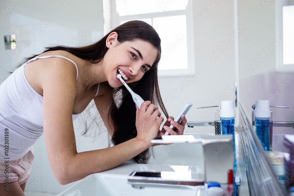 Brunette using smartphone while brushing teeth Brunette using smartphone while brushing teeth