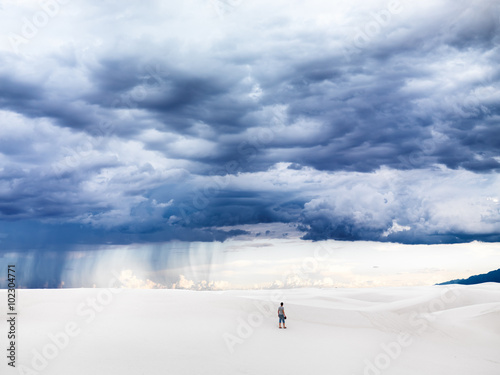lone man standing in vast expanse of white sand with dramatic sky