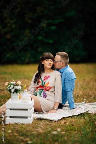 Pregnant beautiful woman with her handsome husband sweetly resting outdoors in the autumn on picnic.