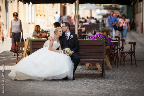 Romantic newlyweds kissing and sitting on wooden bench in old fr