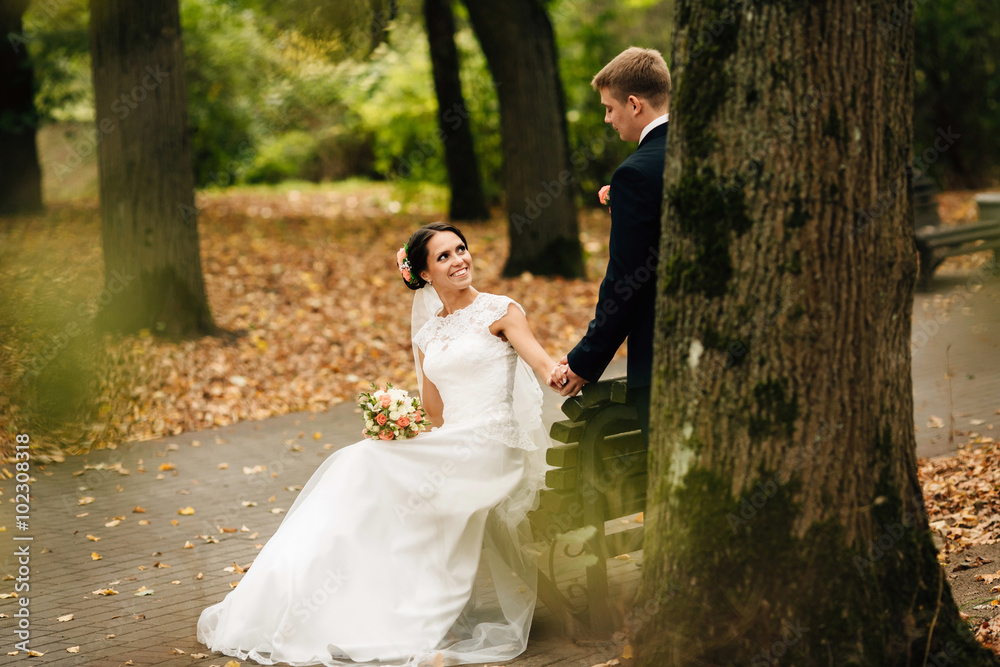 The bride and groom sitting on bench in autumn park
