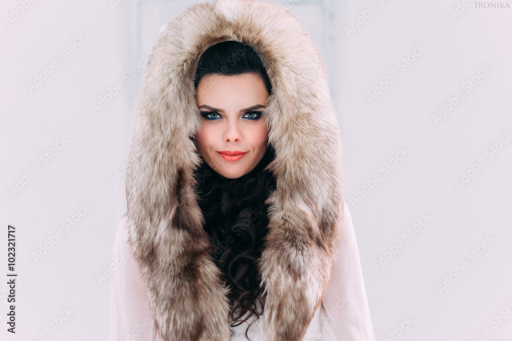 Luxurious brunette in a fur coat with fur hood stands on a snow-covered meadow , fashionable toning , Creative Colors. Luxurious brunette in a fur coat with fur hood stands on a snow-covered meadow , fashionable toning , Creative Colors.