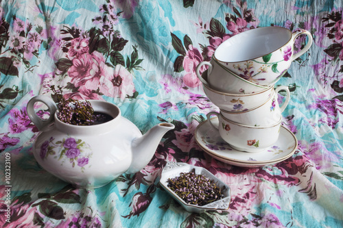 Kettle, set different cups, tea with flowers of heather on fabric background with floral pattern photo