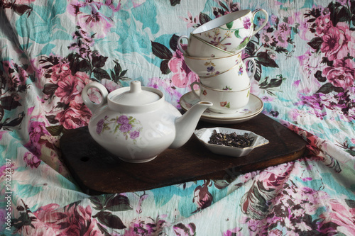 Kettle, set different cups, tea with flowers of heather on fabric background with floral pattern photo