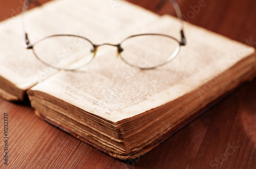 Open old book on wooden table with glasses