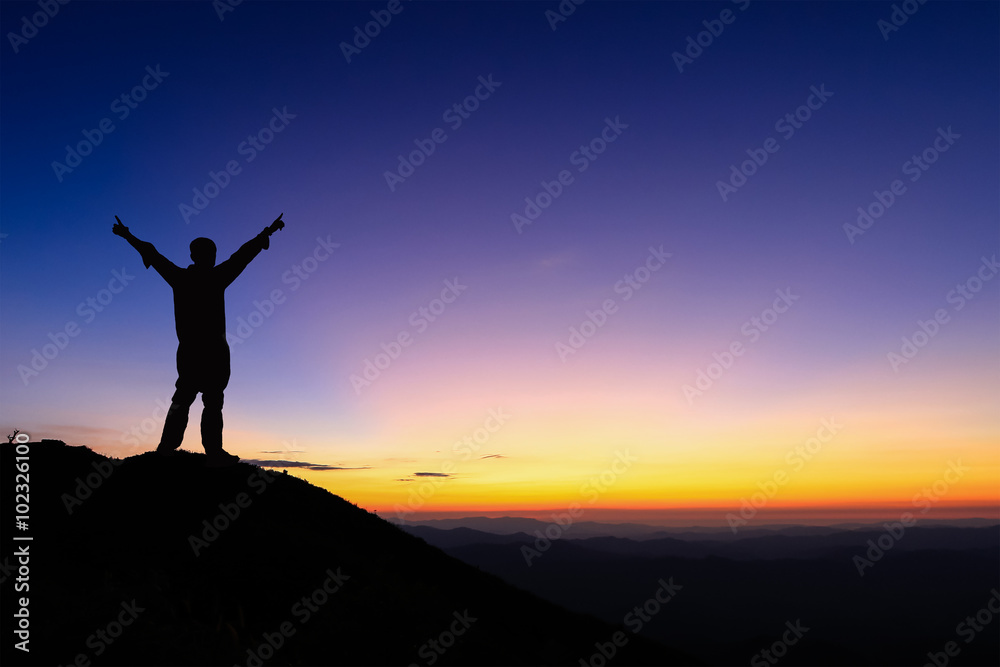 Silhouette of man is standing and spread hand on top of mountain to enjoy colorful sunset sky.