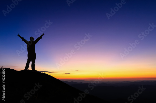 Silhouette of man is standing and spread hand on top of mountain to enjoy colorful sunset sky.