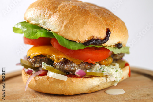 Tasty cheese beef burger with lettuce, cheddar, barbecue sauce, tomatoes, pickles and tzatziki