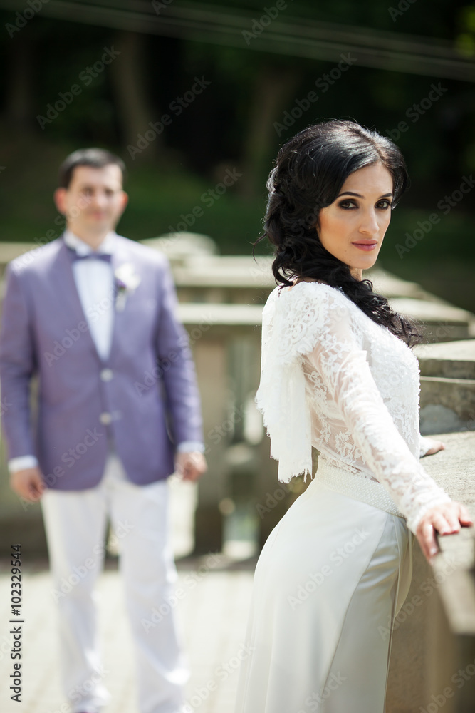 Fototapeta premium Beautiful bride posing on old balcony, groom in background