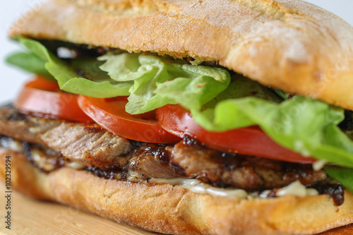 Tasty pork steak sandwich in a ciabatta with tomatos, lettuce, mayonnaise and barbecue sauce