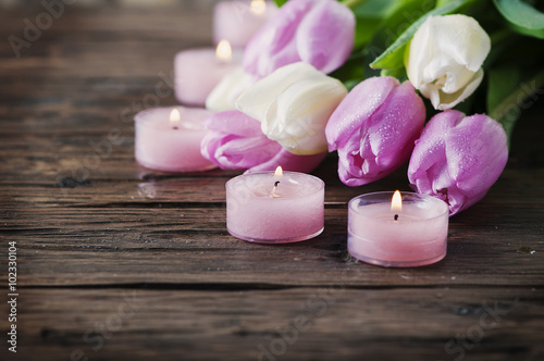 Pink and white tulips and candles on the wooden table