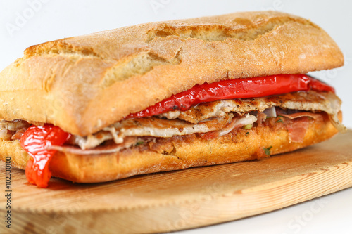 Tasty pork grilled serranito sandwich in a ciabatta with ham and red pepper on a white background