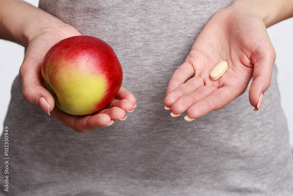 Close up woman's hand holding pills, the other holding an apple Close up woman's hand holding pills, the other holding an apple